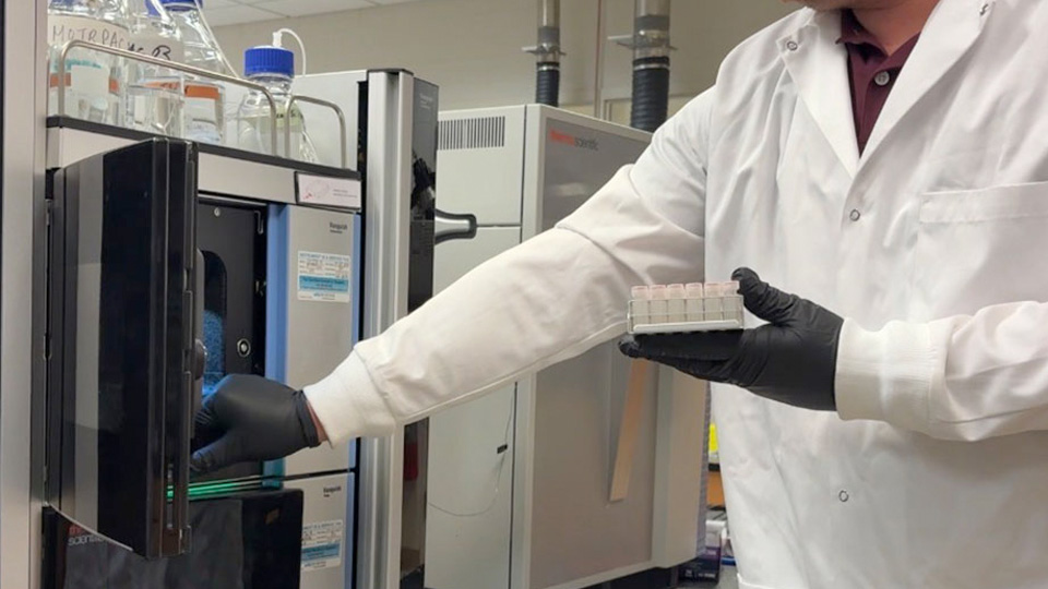 A researcher placing sample vials into a metabolomics analysis instrument.