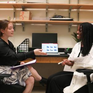 A Project ENGAGES scholar and her mentor sit in a lab and discuss research on papers and on a computer screen.